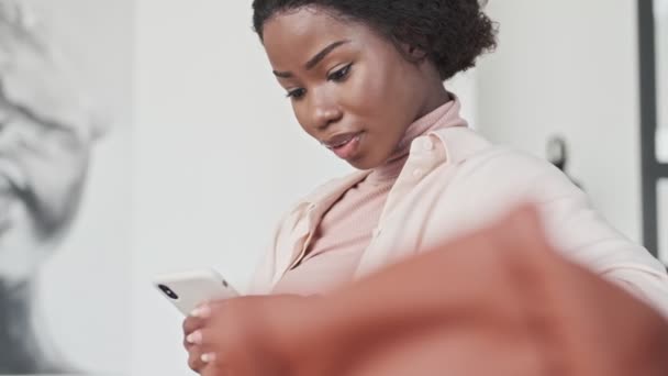 Egy Vidám Fiatal Afrikai Használja Mobilját Miközben Otthon Egy Kanapén — Stock videók