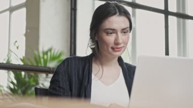 Dost canlısı genç bir iş kadını ofiste çalışırken dizüstü bilgisayarını kullanarak video bağlantısıyla konuşuyor.