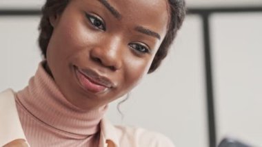 Güzel bir Afrikalı kadının yakın plan görüntüsü evdeki oturma odasında cep telefonundan bir şey izliyor.