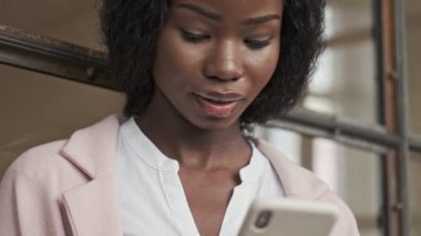 Oldukça sakin bir Afrikalı Amerikalı iş kadını ofisinde akıllı telefonunu kullanıyor.