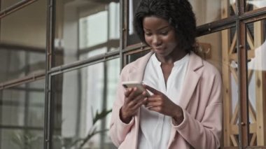 Profesyonel özgüvenli genç bir Afro-Amerikan iş kadını ofiste çalışırken akıllı telefonunu kullanıyor.