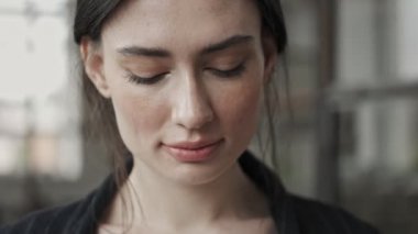 Genç ve sakin bir iş kadınının yakın plan görüntüsü gözlerini açıyor ve ofiste duran kameraya bakıyor.