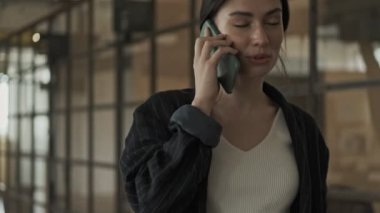 Ofiste yürürken gülümseyen genç bir iş kadını telefonda konuşuyor.