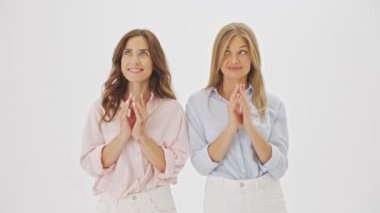 İki çekici kadın stüdyoda beyaz arka planda çılgınca bir şeyler planlıyor.