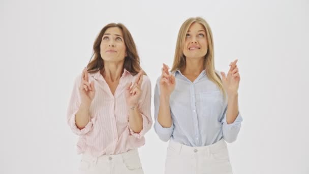 两个漂亮的女人正在祈祷一件事 她们站在一边 交叉着手指 望着工作室里被白色背景隔开的顶部 — 图库视频影像