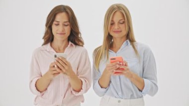 Çekici bir esmer kadın, beyaz arka planda dikilip arkadaşının akıllı telefonuna bakıyor.