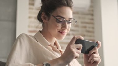 Genç, güzel, mutlu, duygusal bir kadın evde oturuyor ve cep telefonuyla oyunlar oynuyor.