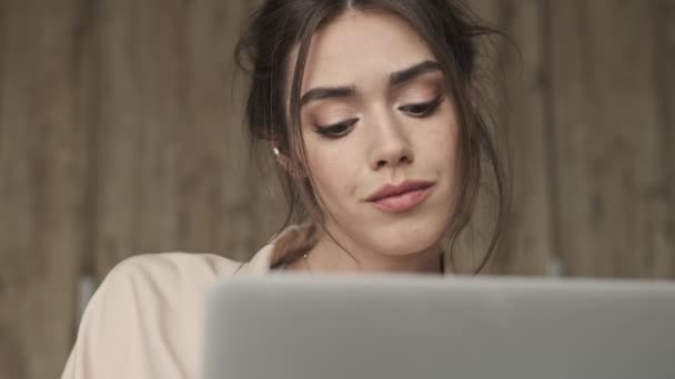 若いかなり美しい女性が自宅でノートパソコンを使用している間に座っている — ストック動画