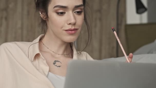 漂亮迷人的女人坐在家里 一边用笔记本电脑 一边用铅笔写便条 — 图库视频影像