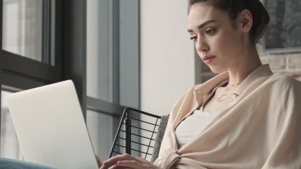아름다운 여성이 집안에 앉아서 컴퓨터를 사용하고 있습니다 — 비디오