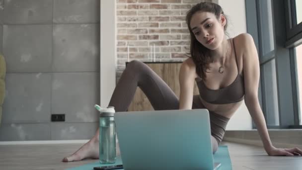 Jovem Mulher Fitness Concentrada Tapete Dentro Casa Usando Computador Portátil — Vídeo de Stock