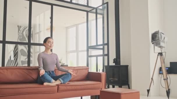 조심스럽고 예쁘게 여성이 집에서 소파에 앉아서 명상하는 — 비디오