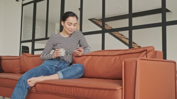 Evdeki Kanepede Otururken Akıllı Telefon Kullanan Neşeli Güzel Asyalı Kadın — Stok video