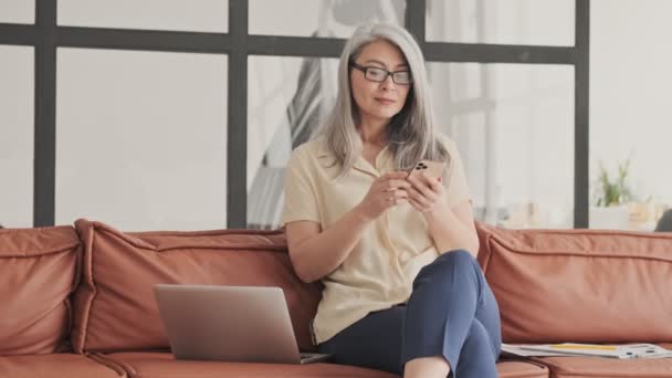 Uzun Gri Saçlı Çekici Bir Kadın Akıllı Telefonunu Dizüstü Bilgisayarını — Stok video