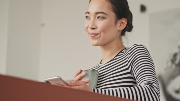 Sorridente Bella Donna Asiatica Utilizzando Smartphone Guardando Lontano Mentre Seduto — Video Stock