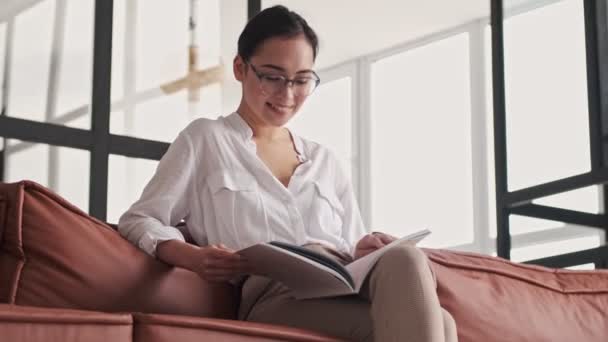 Smiling Elegant Pretty Asian Woman Eyeglasses Reading Magazine Looking Away — стоковое видео