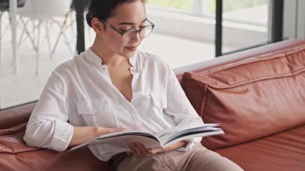 Enfocado Elegante Bastante Asiático Mujer Gafas Lectura Revista Mientras Sentado — Vídeo de stock