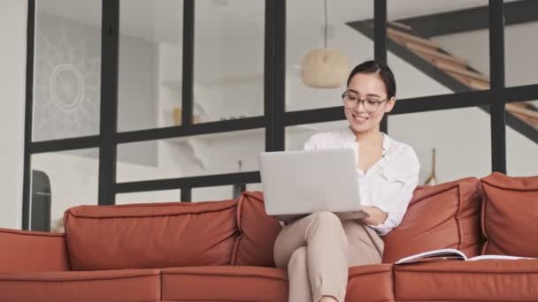 Mutlu Zarif Gözlüklü Asyalı Kadın Evde Kanepede Otururken Dizüstü Bilgisayar — Stok video