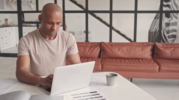 一位严肃的非洲裔美国人正在家中客厅里与笔记本电脑一起工作 — 图库视频影像