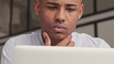 Ciddi bir Afrikalı Amerikalı 'nın yakın plan görüntüsü evinde oturan gümüş dizüstü bilgisayarına bakıyor.