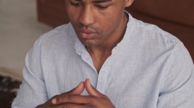 Ciddi düşünen Afro-Amerikan bir adamın yakından çekilmiş görüntüsü evdeki oturma odasında çalışıyor.