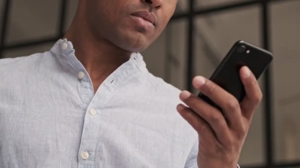 真剣に焦点を当てたアフリカ系アメリカ人の男性が自宅のリビングルームでスマートフォンを持っています — ストック動画