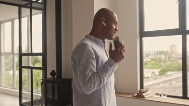 Happy Pleased African American Man Talking Phone Using Wireless Earphones — Stock Video