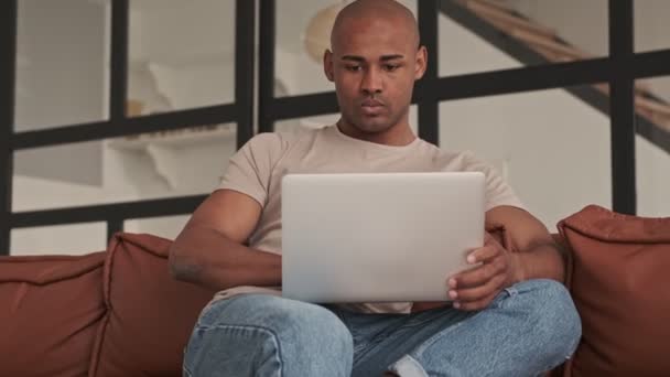 Сосредоточенный Африке Мужчина Использует Ноутбук Сидя Дома Диване Гостиной — стоковое видео
