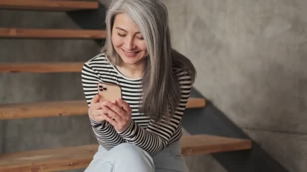 Usmívající Stará Žena Používá Svůj Smartphone Sedí Schodišti Obývacím Pokoji — Stock video