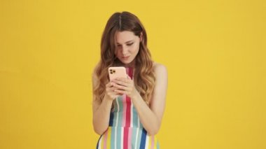Canı sıkkın bir kadın, sarı arka planda tek başına duran akıllı telefonuna mesaj yazıyor.