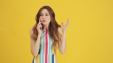 Şok olmuş bir kadın akıllı telefonuyla konuşuyor sarı arka planda tek başına duruyor.