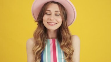 Pembe şapkalı hoş bir genç kadın sarı bir arka planda izole bir şekilde poz veriyor.