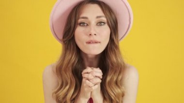 Duygusal olarak şaşırmış pembe şapkalı genç bir kadının yakından görüntüsü sarı bir arka planda izole edilmiş sevinç dolu.