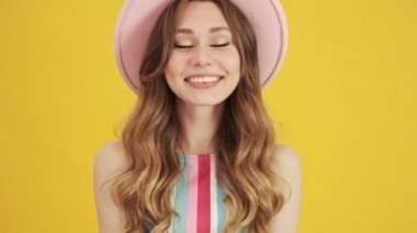 Pembe şapkalı mutlu genç bir kadının yakın çekim görüntüsü sarı arka planda izole edilmiş kameraya hava öpücüğü gönderiyor.