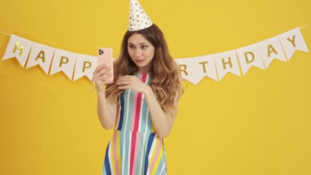 Emocjonalnie Podekscytowana Urodzinowa Kobieta Rozmawia Swoim Smartfonie Stojąc Żółtym Tle — Wideo stockowe