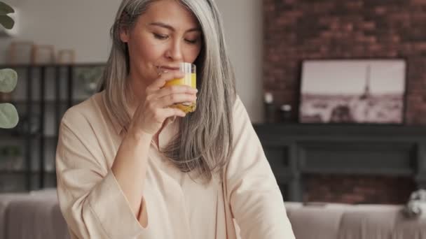Μια Χαμογελαστή Ώριμη Γυναίκα Πίνει Χυμό Πορτοκάλι Στην Κουζίνα Στο — Αρχείο Βίντεο