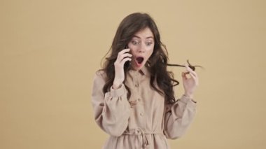 Gülen bir kadın telefonuyla konuşuyor. Bej bir arka planda tek başına duruyor.