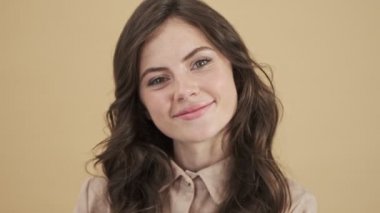 Mutlu gülümseyen bir kadının yakın plan görüntüsü bej bir arkaplan üzerinden izole edilmiş kameraya poz veriyor.