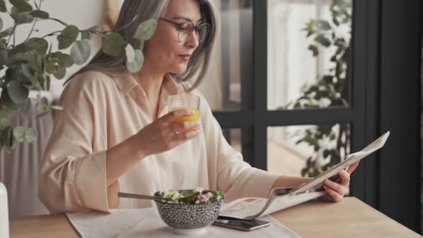 Eine Lächelnde Reife Frau Mit Brille Liest Eine Zeitung Während — Stockvideo