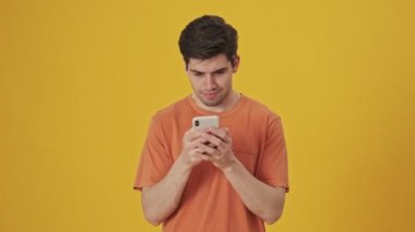 Akıllı telefon kullanarak tişört giyen ve sarı arka planda mutlu olan gülümseyen yakışıklı adam.