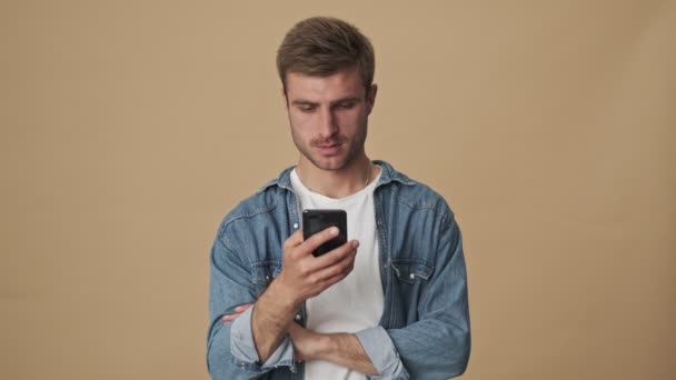 Joven Guapo Está Usando Teléfono Inteligente Mientras Hace Gesto Ganador — Vídeo de stock