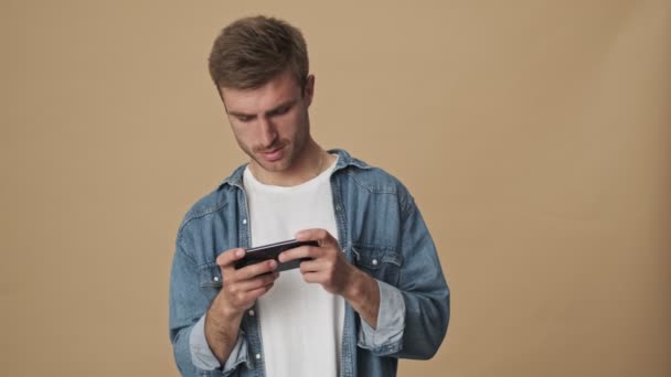 Joven Enfocado Está Jugando Juego Teléfono Inteligente Sosteniéndolo Horizontalmente Pie — Vídeos de Stock