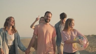 Gülümseyen bir arkadaş grubu kumsalda yürüyor.