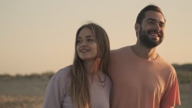 Güzel, gülümseyen bir çift kumsalda yürüyorlar ve sarılıyorlar.