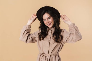 Şapkalı, gülümseyen ve bej arka planda izole edilmiş kameraya bakan mutlu beyaz kadın görüntüsü.