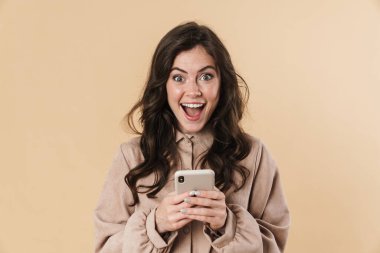 Bej arka planda izole edilmiş, gülümseyen ve cep telefonunda yazan neşeli bir kadın resmi