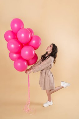 Bej arka planda izole edilmiş pembe balonlarla poz verirken gülümseyen güzel bir kadın görüntüsü