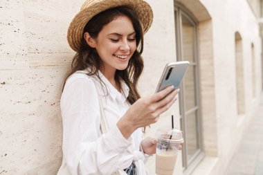 Şehir caddesinde yürürken cep telefonu kullanan ve milkshake içen genç kadının portresi.