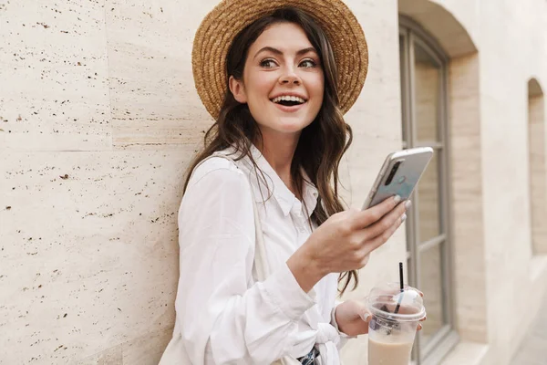 街を歩きながら携帯電話を使いミルクシェイクを飲む若い喜びの女性の肖像画 — ストック写真