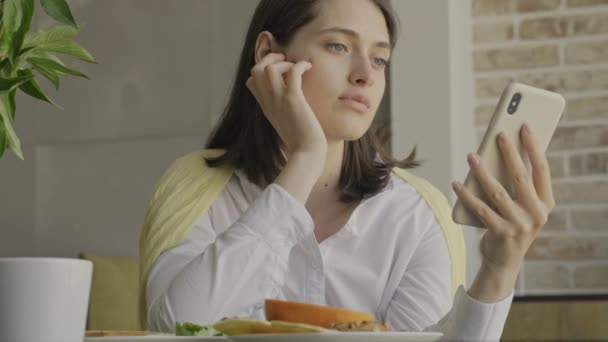 朝食をとりながら携帯電話を使って家の中ですごい集中力のある女性 — ストック動画